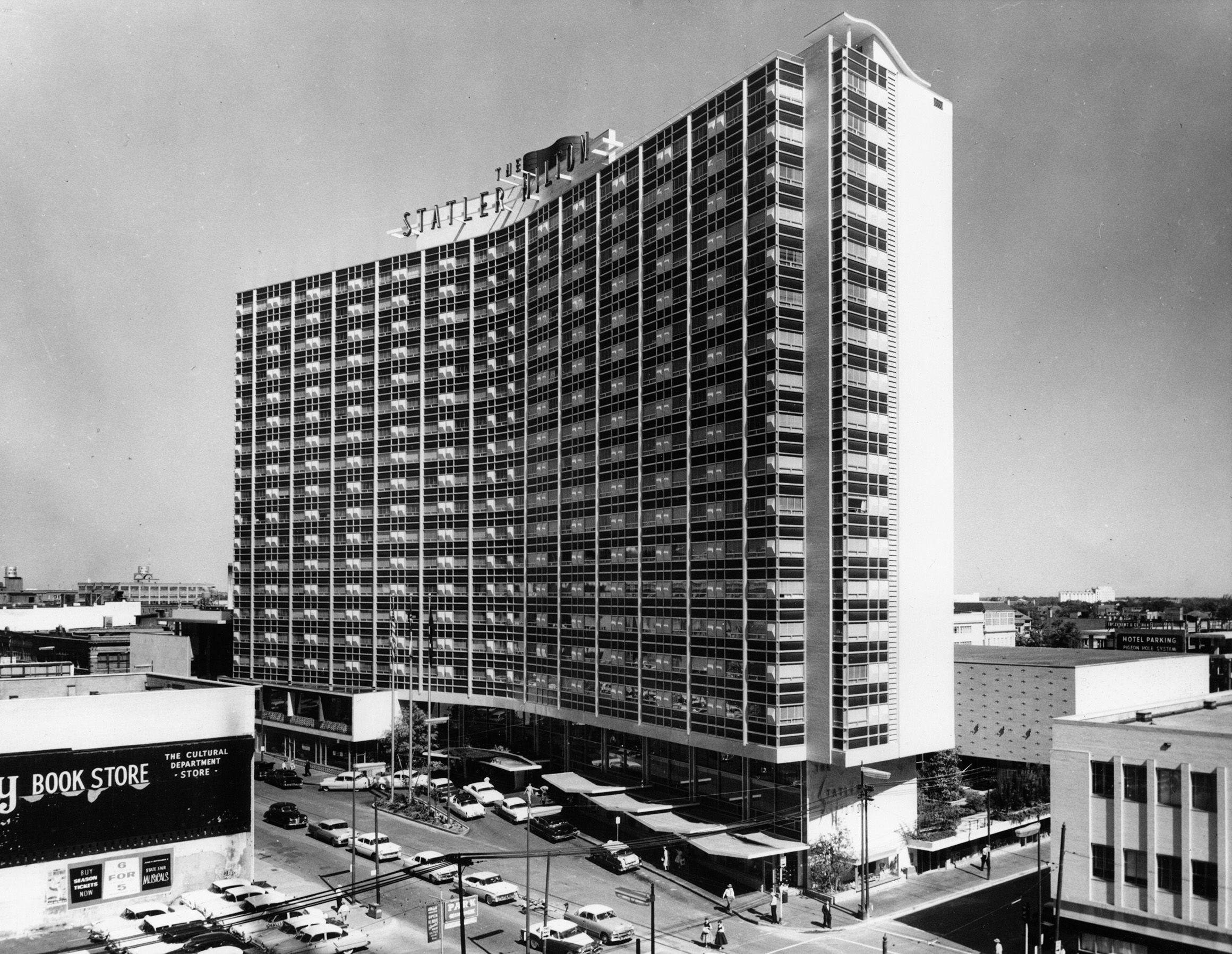 Archival black-and-white photograph of the Statler Hilton hotel in downtown Dallas, circa 1960, with its rooftop sign and mid-century cars on the street below